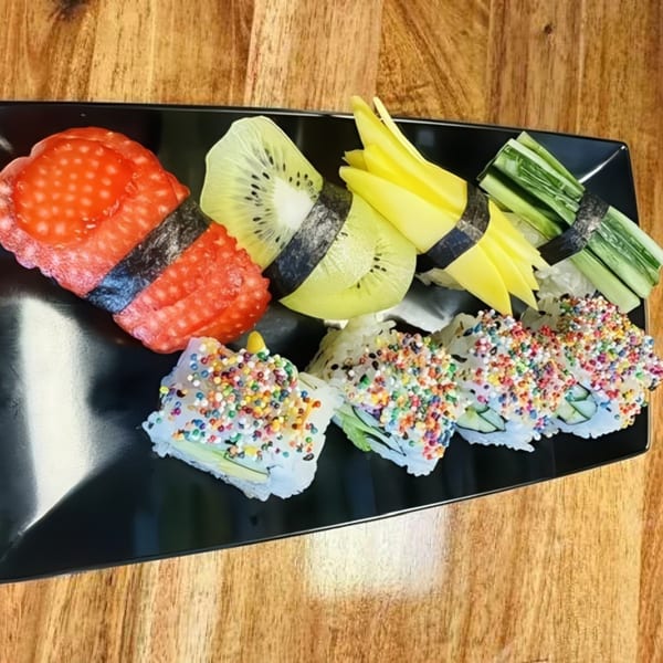 Colorful sushi rolls with fruit toppings and sprinkles on a black plate.