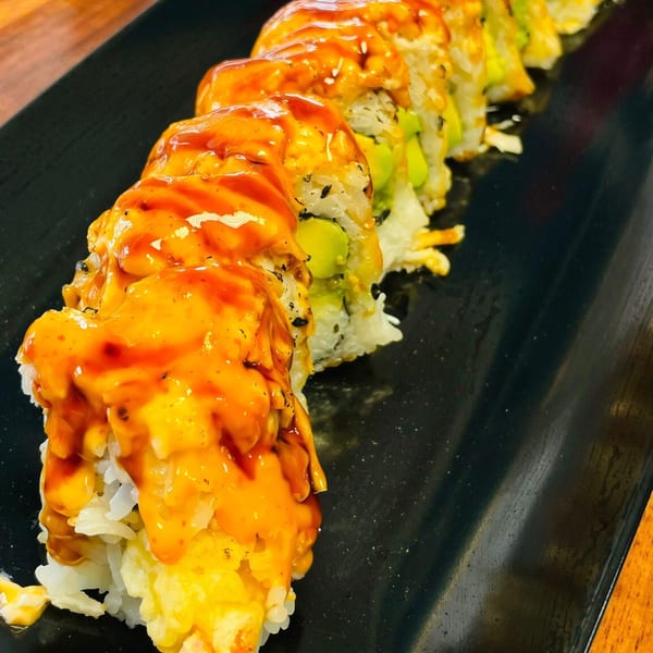 A row of My Sushi & Catering LLC sushi rolls topped with orange and red sauces on a black plate.