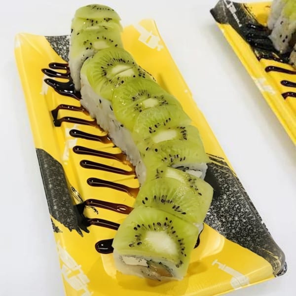 Kiwi sushi roll with dark sauce drizzle on a yellow and black patterned plate from My Sushi & Catering.
