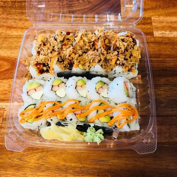 Assorted sushi rolls in a clear plastic container, including crispy, avocado, and spicy mayo varieties.